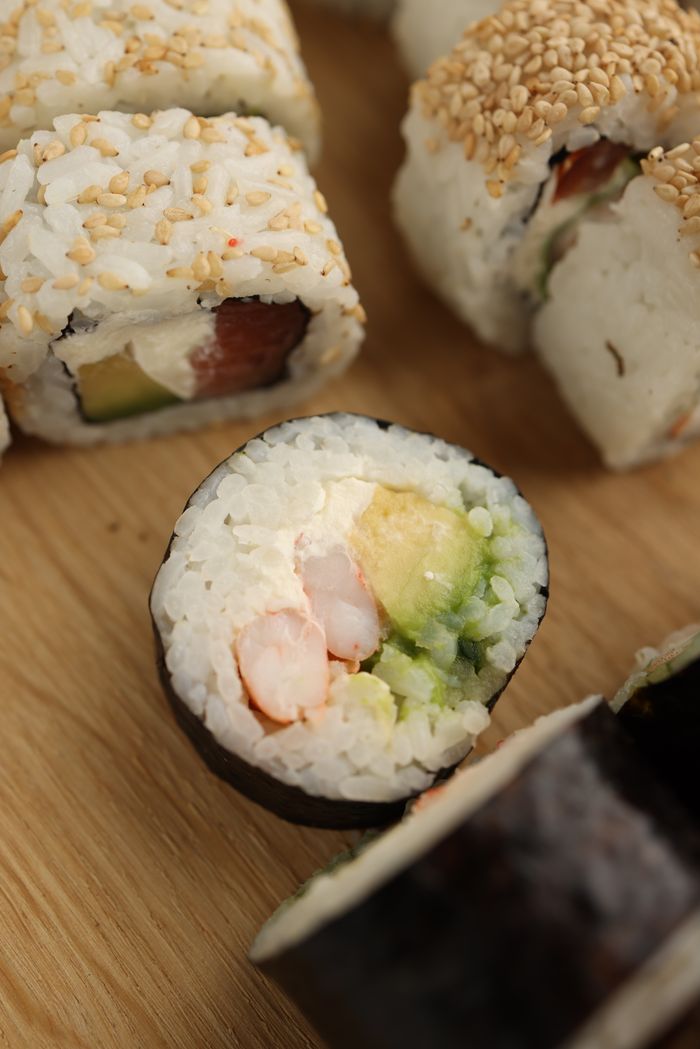 Home Close-up of sushi rolls featuring fresh avocado and seafood on a wooden board.