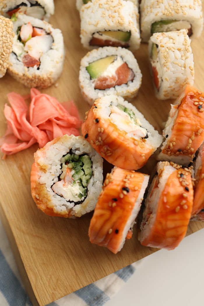 Home A delicious assortment of sushi rolls served on a wooden board with pickled ginger.