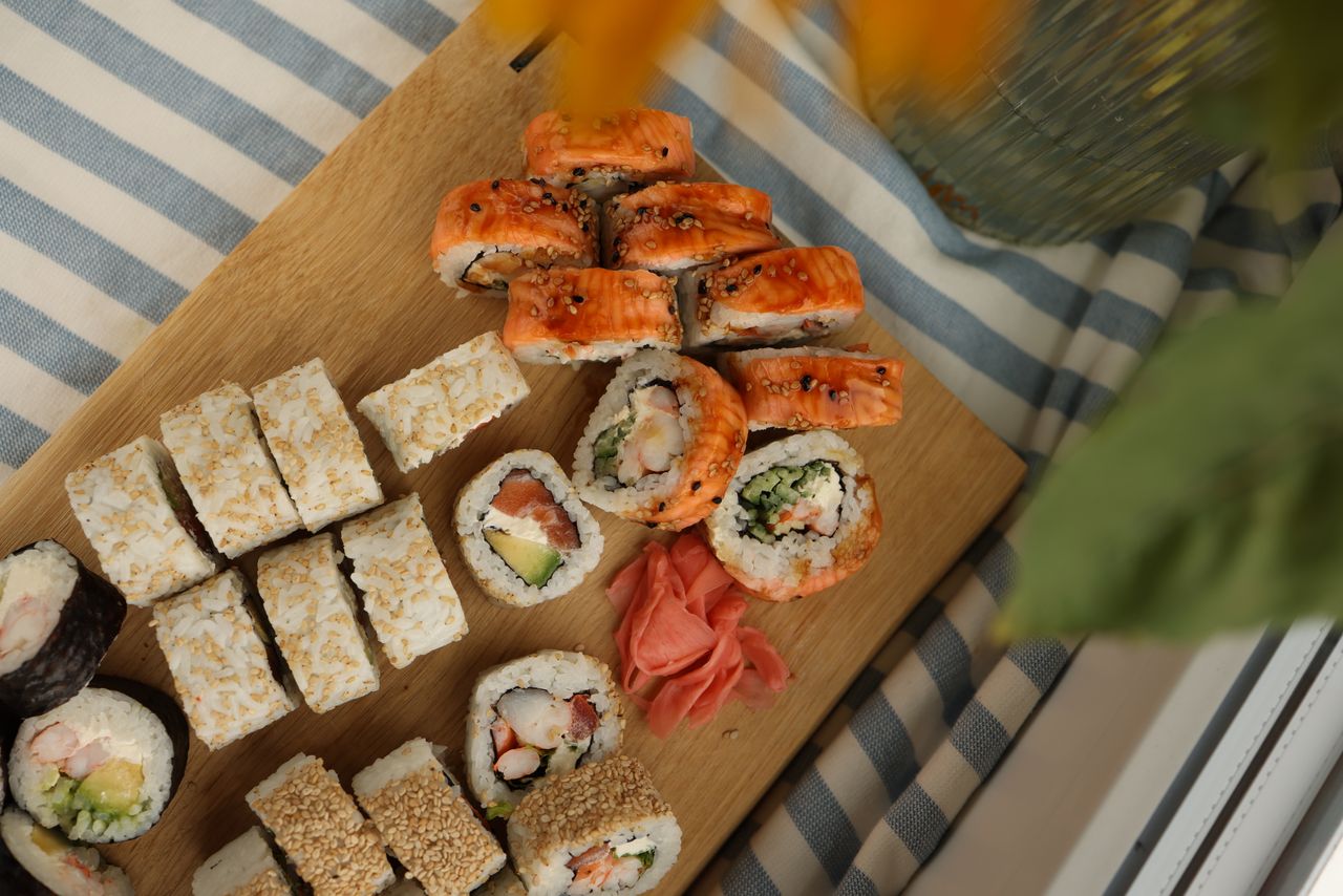 Home Top view of assorted sushi rolls with ginger on a wooden board.