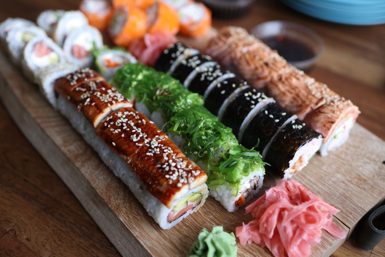 Home A delicious selection of sushi rolls with toppings like seaweed and sesame seeds on a wooden platter.