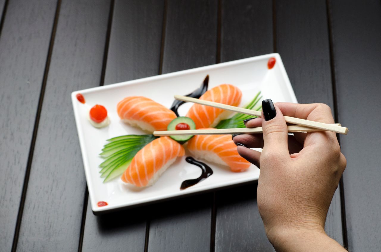 Home Close-up of a sushi plate with salmon nigiri and decorative garnish, held with chopsticks.